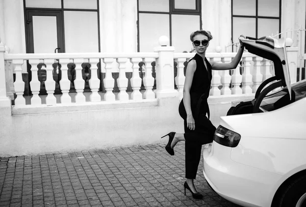 Foto al aire libre de moda de mujer hermosa sexy con pelo oscuro en chaqueta de cuero negro y gafas de sol posando en auto de lujo — Foto de Stock