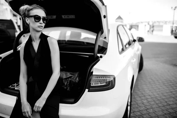 Foto al aire libre de moda de mujer hermosa sexy con pelo oscuro en chaqueta de cuero negro y gafas de sol posando en auto de lujo — Foto de Stock