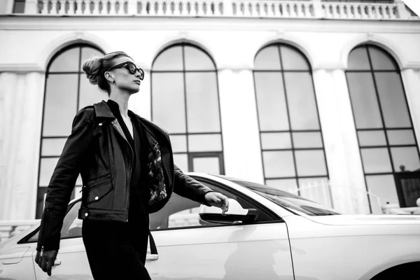 Moda foto ao ar livre de mulher bonita sexy com cabelo escuro em jaqueta de couro preto e óculos de sol posando em auto luxuoso — Fotografia de Stock