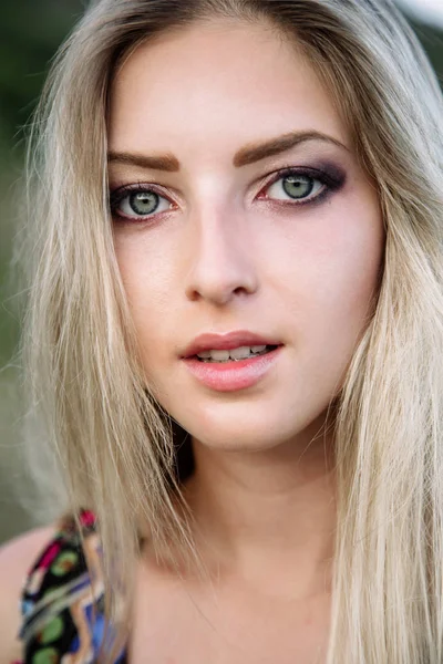 Portræt af en smuk blondine med smukke øjne i blå overalls i naturen, den nedgående sol - Stock-foto