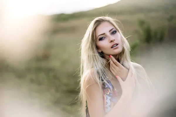 Beautiful blonde with beautiful eyes in blue overalls in nature, sunset sun — Stock Photo, Image