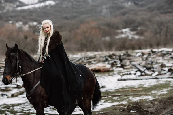 Schöne blonde Wikinger in einem schwarzen Umhang zu Pferd — Stockfoto