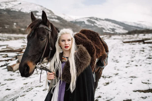 Hermosa rubia vikinga en una capa negra a caballo — Foto de Stock