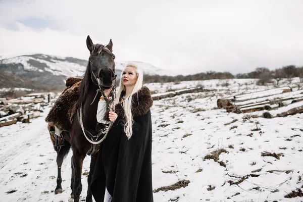 Hermosa rubia vikinga en una capa negra a caballo — Foto de Stock