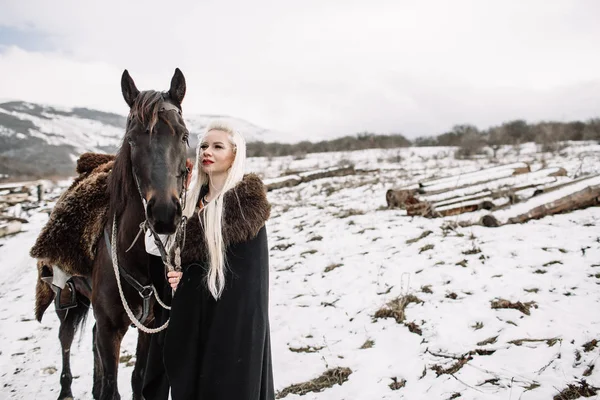 Hermosa rubia vikinga en una capa negra a caballo — Foto de Stock