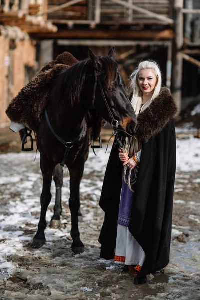 Портрет молодої блондинки в чорному плащі з конем . — стокове фото
