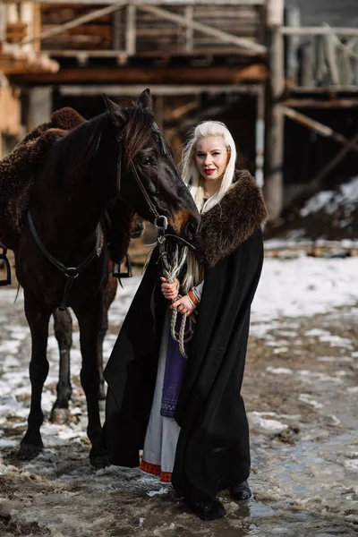 Портрет молодої блондинки в чорному плащі з конем . — стокове фото