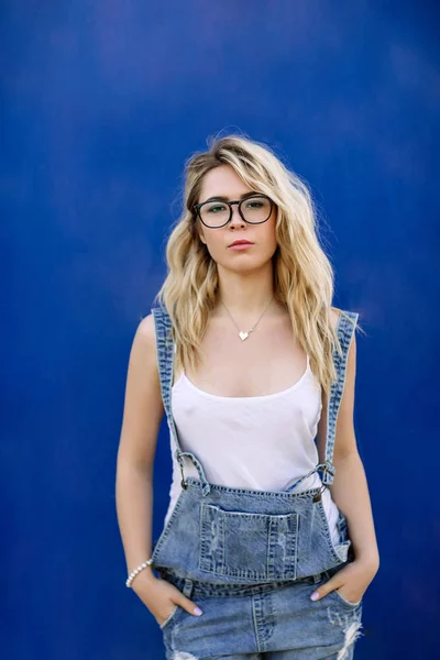 Mladé stylové plavovláska v džínové oděvy vyrobené z džínoviny a na modrém pozadí — Stock fotografie