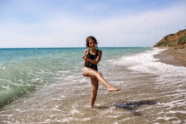 Alta moda look.glamor hermosa sexy elegante modelo femenino joven morena con maquillaje brillante, con perfecto tomar el sol limpia la piel en un traje de baño negro en la playa en el estilo de moda —  Fotos de Stock