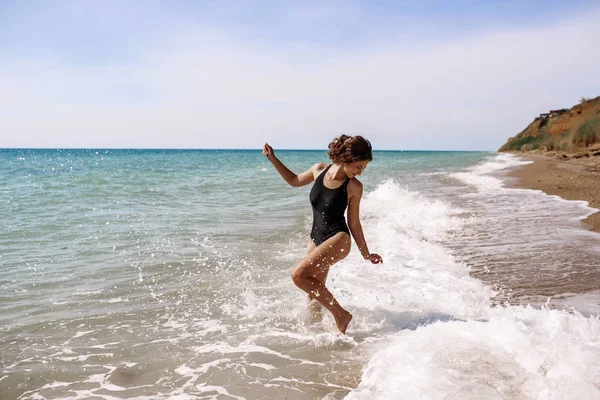 Alta moda look.glamor hermosa sexy elegante modelo femenino joven morena con maquillaje brillante, con perfecto tomar el sol limpia la piel en un traje de baño negro en la playa en el estilo de moda —  Fotos de Stock