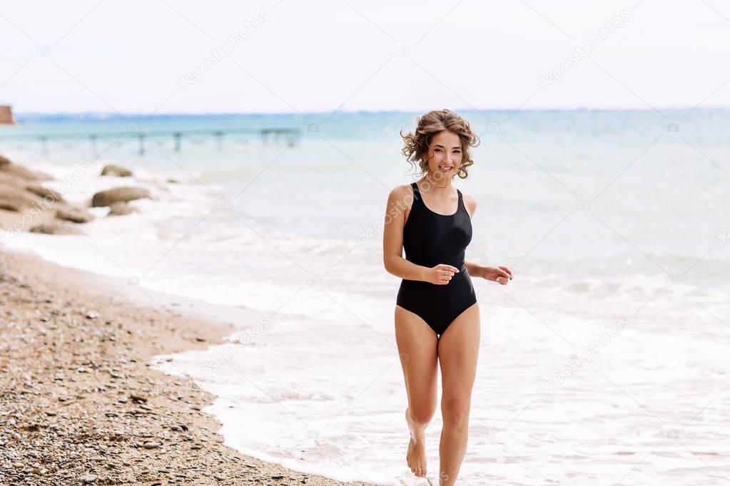 High fashion look.glamor beautiful sexy stylish brunette young female model with bright make-up, with perfect sunbathing clean skin in a black swimsuit on the beach in fashion style