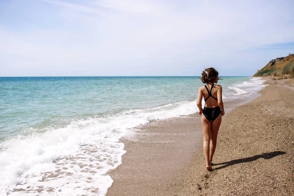 Alta moda look.glamor hermosa sexy elegante modelo femenino joven morena con maquillaje brillante, con perfecto tomar el sol limpia la piel en un traje de baño negro en la playa en el estilo de moda —  Fotos de Stock