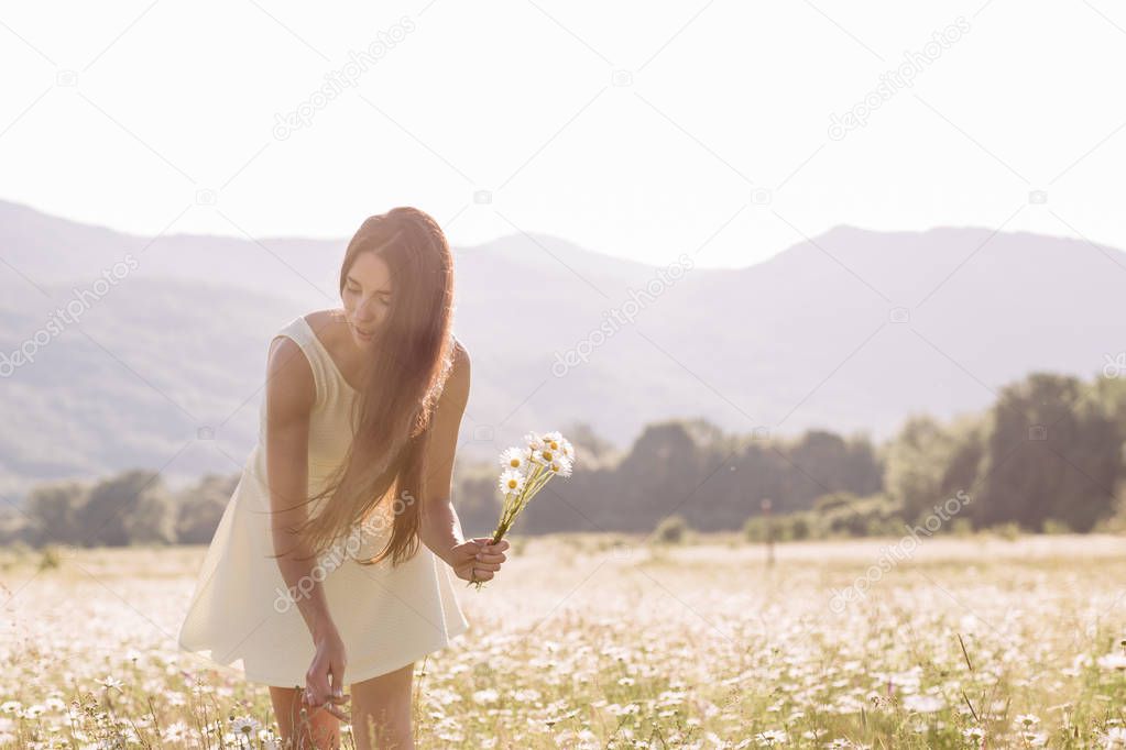 Beautiful woman enjoying a field of daisies, beautiful woman lying in a meadow of flowers, beautiful girl relaxing outdoors, having fun, holding plant, happy young lady and spring-green nature, harmon