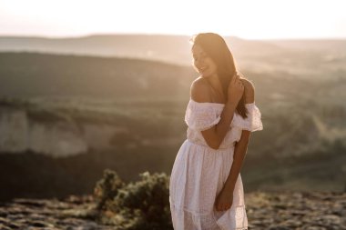 Güzel kız bir dağın tepesinde kalır ve horizon adlı güzel bir arka plan ile görünüyor. Doğal bir günbatımı, inanılmaz bir mucize renkli bir fotoğrafı, bir dans, Rüzgar saçlarında