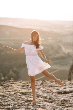 Güzel kız bir dağın tepesinde kalır ve horizon adlı güzel bir arka plan ile görünüyor. Doğal bir günbatımı, inanılmaz bir mucize renkli bir fotoğrafı, bir dans, Rüzgar saçlarında