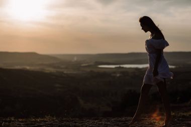 Güzel kız bir dağın tepesinde kalır ve horizon adlı güzel bir arka plan ile görünüyor. Doğal bir günbatımı, inanılmaz bir mucize renkli bir fotoğrafı, bir dans, Rüzgar saçlarında
