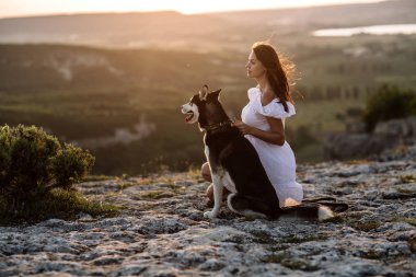 Gün batımında dağlarda bir köpek (siyah ve beyaz husky mavi gözlü) ile güzel kız çalış