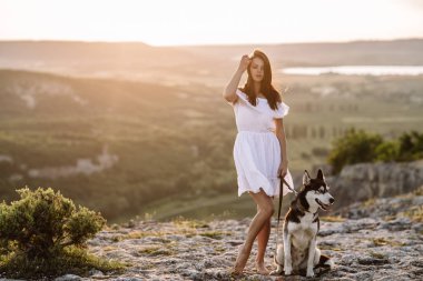 Gün batımında dağlarda bir köpek (siyah ve beyaz husky mavi gözlü) ile güzel kız çalış