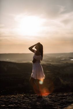 Güzel kız bir dağın tepesinde kalır ve horizon adlı güzel bir arka plan ile görünüyor. Doğal bir günbatımı, inanılmaz bir mucize renkli bir fotoğrafı, bir dans, Rüzgar saçlarında