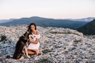 Gün batımında dağlarda bir köpek (siyah ve beyaz husky mavi gözlü) ile güzel kız çalış