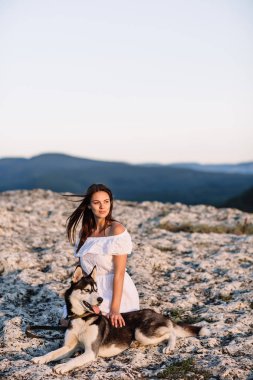 Gün batımında dağlarda bir köpek (siyah ve beyaz husky mavi gözlü) ile güzel kız çalış