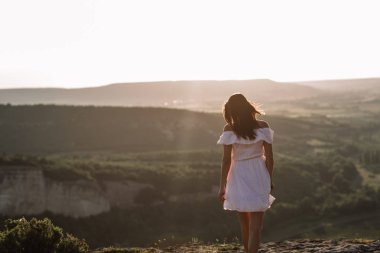 Güzel kız bir dağın tepesinde kalır ve horizon adlı güzel bir arka plan ile görünüyor. Doğal bir günbatımı, inanılmaz bir mucize renkli bir fotoğrafı, bir dans, Rüzgar saçlarında