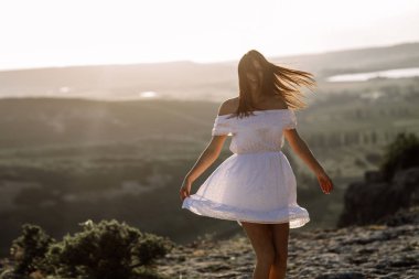 Güzel kız bir dağın tepesinde kalır ve horizon adlı güzel bir arka plan ile görünüyor. Doğal bir günbatımı, inanılmaz bir mucize renkli bir fotoğrafı, bir dans, Rüzgar saçlarında