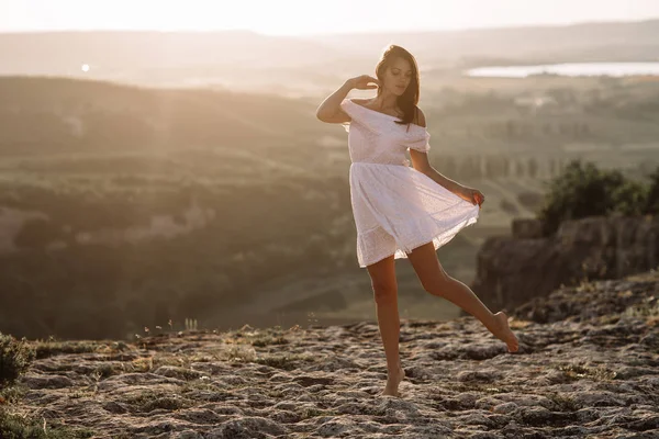 Menina bonita permanece no topo de uma montanha e olha para o horizonte com um belo fundo. Uma foto colorida de um pôr-do-sol natural, um milagre, incrível, uma dança, cabelo ao vento — Fotografia de Stock