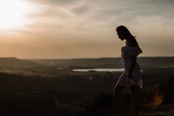 Vacker flicka är fortfarande på toppen av ett berg och tittar på horisonten med en vacker bakgrund. En färgglad bild av en naturlig solnedgång, ett mirakel, otrolig, en dans, hår i vinden — Stockfoto