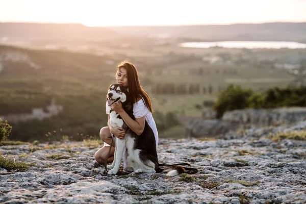 Gün batımında dağlarda bir köpek (siyah ve beyaz husky mavi gözlü) ile güzel kız çalış