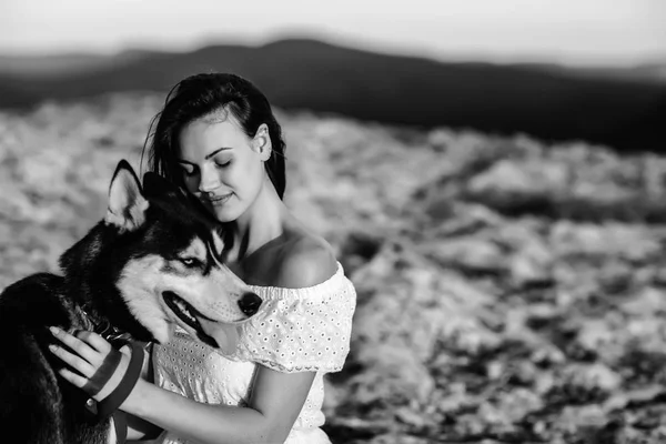美しい少女は日没で山の犬 (黒と白青い目のハスキー) と遊ぶ — ストック写真