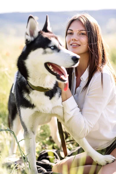 美しい少女が犬 (黒と白青い目のハスキー) グリーン フィールドで遊ぶ — ストック写真