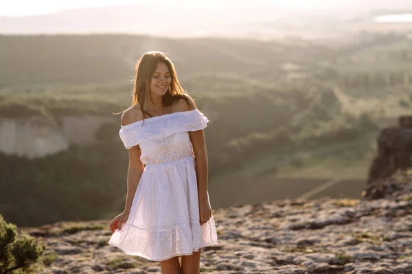 Belle fille reste au sommet d'une montagne et regarde l'horizon avec un beau fond. Une photo colorée d'un coucher de soleil naturel, un miracle, incroyable, une danse, les cheveux dans le vent — Photo