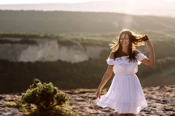 Belle fille reste au sommet d'une montagne et regarde l'horizon avec un beau fond. Une photo colorée d'un coucher de soleil naturel, un miracle, incroyable, une danse, les cheveux dans le vent — Photo