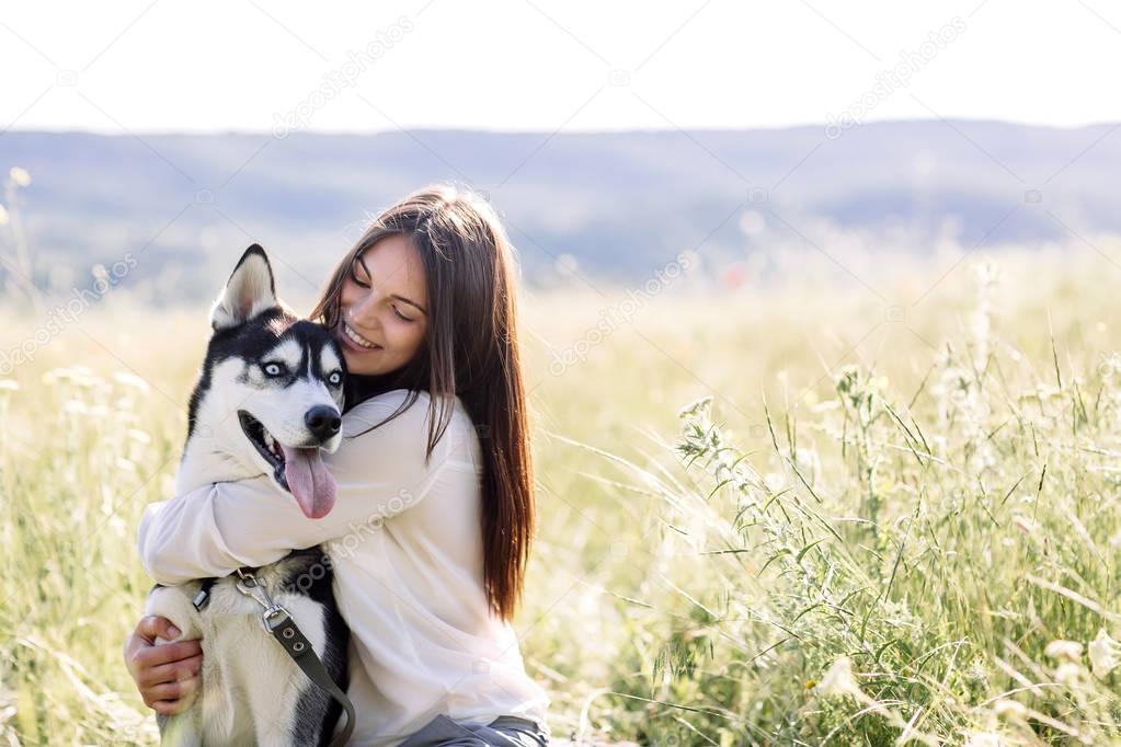 Beautiful girl plays with a dog (black and white husky with blue eyes) green field