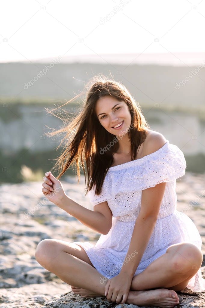 Beautiful girl remains on top of a mountain and looks at the horizon with a beautiful background. A colorful photo of a natural sunset, a miracle, incredible, a dance, hair in the wind
