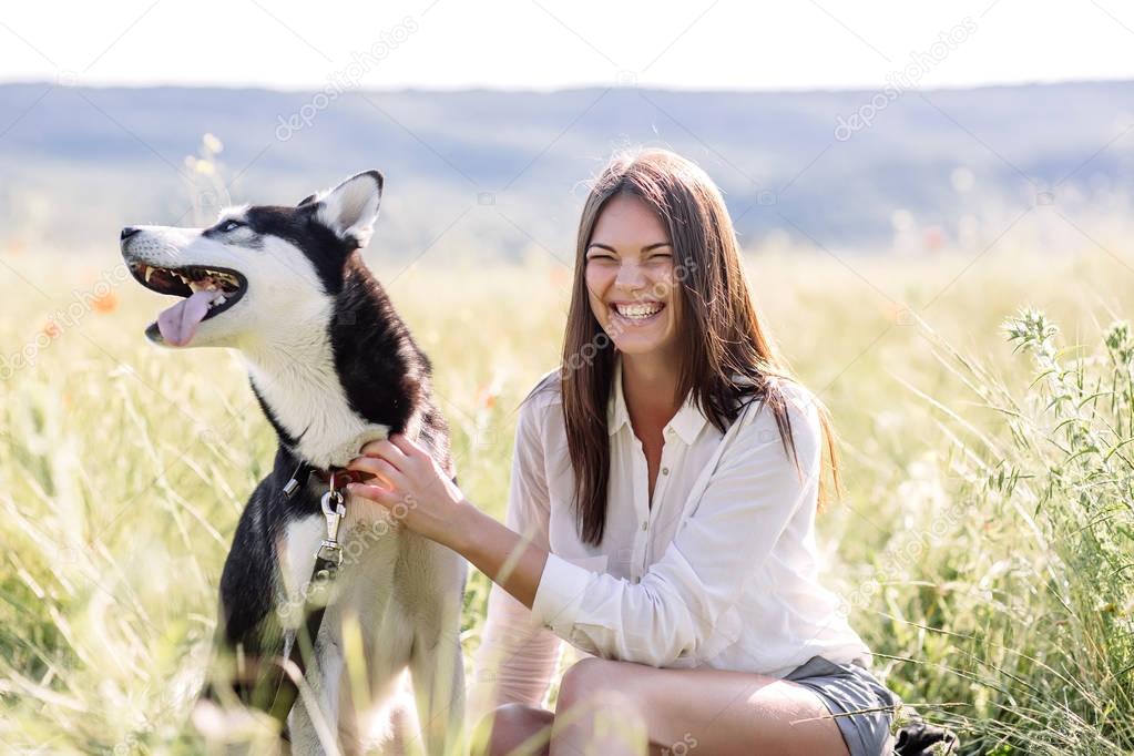 Beautiful girl plays with a dog (black and white husky with blue eyes) green field
