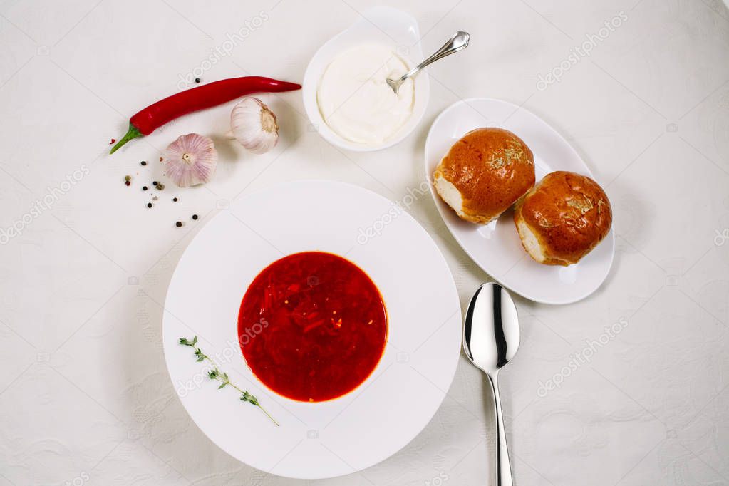 Ukrainian and Russian traditional beet soup - borscht in a white plate with sour cream, spices, garlic, red pepper, dried herbs and pampushkas on a white dish, healthy food.