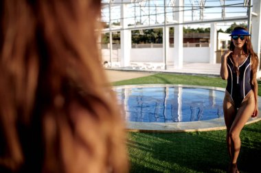 Güzel esmer kız uzun sarı saçlı ve esmer ile iyi durumda bir beyaz mayo mükemmel cilt, havuzun mavi su, yumuşak bir gülümseme ile açık gözler holding ile yalan söylüyor