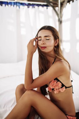 Bikini modeli. Güzel seksi esmer kız modeli uzun dalgalı saçlı, güneş yanığı sahilde moda mayo giyiyor. Tatil. Yanık tenli kadın.