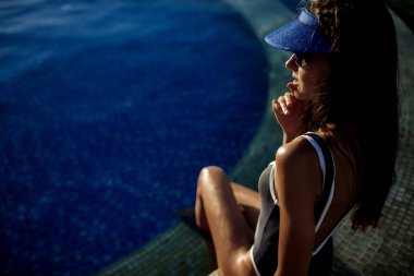 Güzel esmer kız uzun sarı saçlı ve esmer ile iyi durumda bir beyaz mayo mükemmel cilt, havuzun mavi su, yumuşak bir gülümseme ile açık gözler holding ile yalan söylüyor