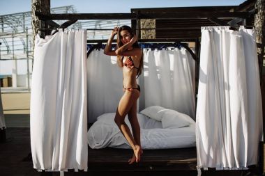 Bikini modeli. Güzel seksi esmer kız modeli uzun dalgalı saçlı, güneş yanığı sahilde moda mayo giyiyor. Tatil. Yanık tenli kadın.