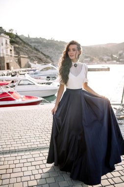 Güzel kız iskelede yürüyüş tarafından denize yakın yat, tekne mavi uzun elbise