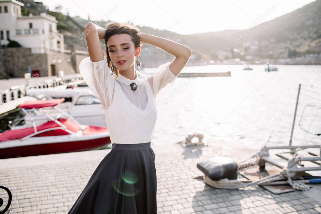 Beautiful girl walking on the pier by the sea near the yacht, boats in the blue long dress