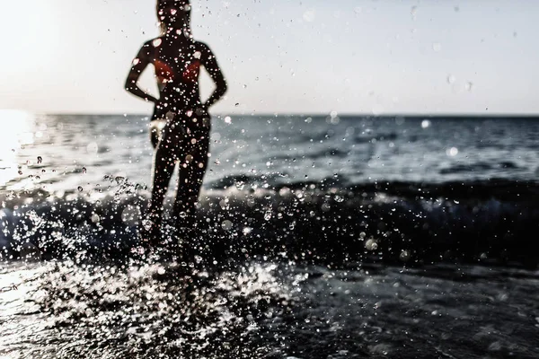 Prise de vue rétroéclairée de la fille courant les jambes dans l'eau à la plage par une journée ensoleillée en été. éclaboussures d'eau — Photo