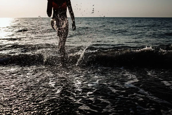 Yaz aylarında güneşli bir günde bacaklarını plajda su ile çalışan kız arkadan aydınlatmalı vurdu. su sıçraması