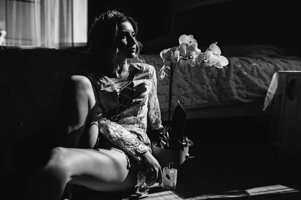 Όμορφη γυναίκα εσώρουχα δείχνει μακρά πόδια σέξι πόζα που ακουμπά στο κρεβάτι πάνω από την κρεβατοκάμαρά της με μεγάλο παράθυρο, λουλούδια. Σεξουαλικές αναμνήσεις. Νύφη μπουντουάρ. Γάμος πρωί. — Φωτογραφία Αρχείου