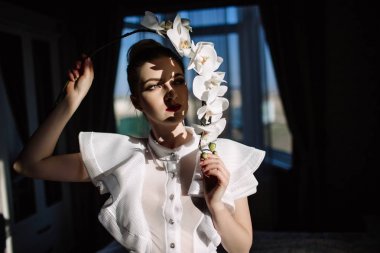 Güzel sarışın kız tutan orkide, sert güneş ışığı, moda