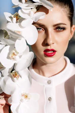 Güzel sarışın kız tutan orkide, sert güneş ışığı, moda