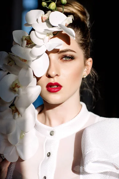 Güzel sarışın kız tutan orkide, sert güneş ışığı, moda